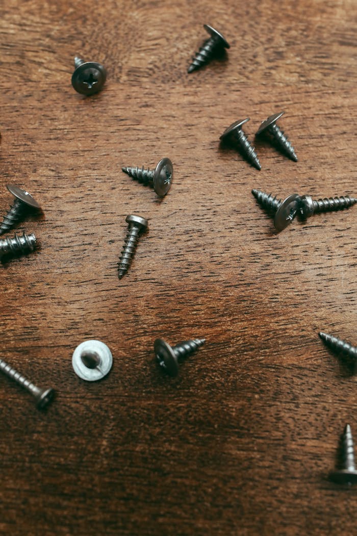 impact-img Detailed image of metal screws scattered on a wooden surface, ideal for carpentry-themed projects.